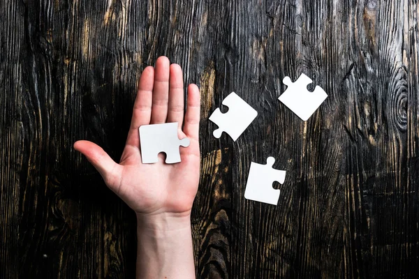 Pieces of jigsaw on table and on palm — Stock Photo, Image