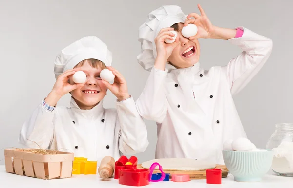 Kleine jongen en meisje in cook vorm houden van eieren — Stockfoto