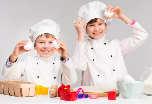 Kleine jongen en meisje in cook vorm houden van eieren — Stockfoto