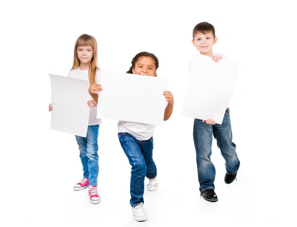 Tres niños divertidos sosteniendo espacios en blanco de papel en las manos — Foto de Stock