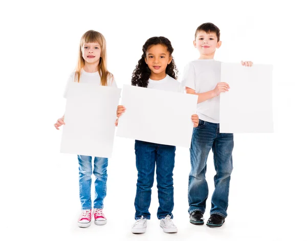 Tres niños divertidos sosteniendo espacios en blanco de papel en las manos — Foto de Stock