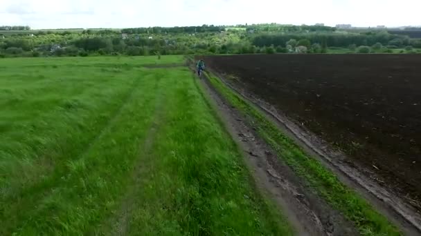 Girl riding on bike from village across field — Stock Video