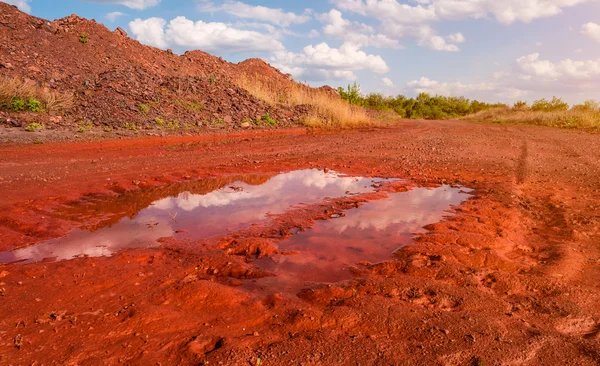 Flaque d'eau dans le sentier sur terre rouge — Photo