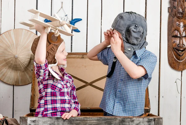 Маленька дівчинка з дерев'яним літаком в руці і хлопчик в пілотному капелюсі — стокове фото