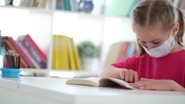Kis iskolás lány védő maszk olvasókönyv — Stock videók