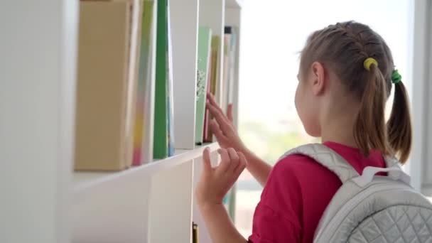 Glad skolflicka söker bok i biblioteket — Stockvideo