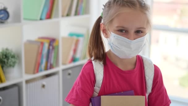 Niña en máscara protectora sosteniendo libros de texto — Vídeo de stock