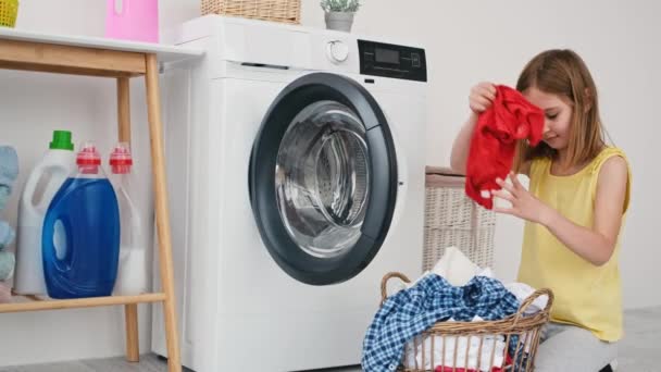 Liten flicka lastar kläder i tvättmaskin — Stockvideo