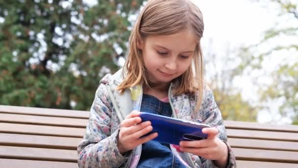 Little girl gaming on smartphone outdoors — Stock Video