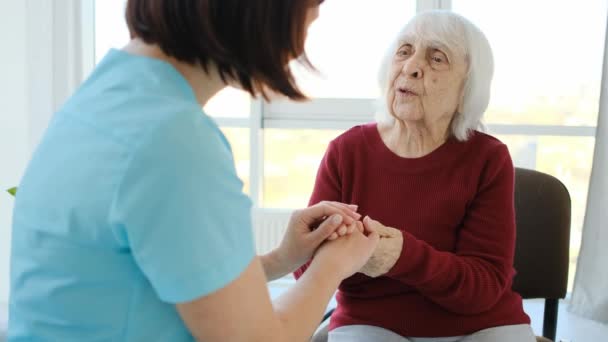 У віці жінка розмовляє з медсестрою, тримаючи руки — стокове відео
