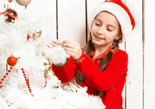 Klein meisje in rood santa hoed versieren nieuwjaar boom — Stockfoto