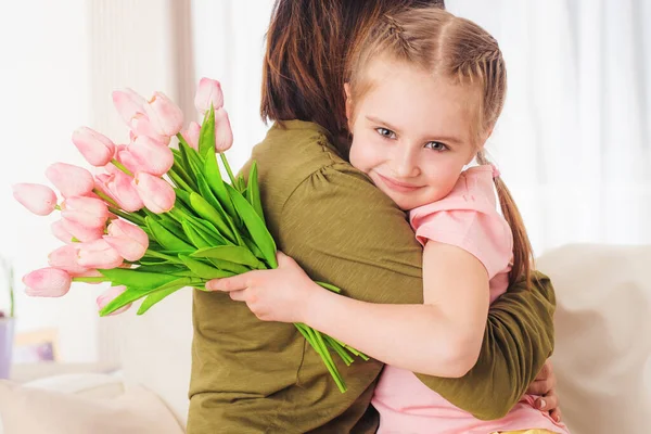 Kind umarmt Mutter, hält Blumen — Stockfoto