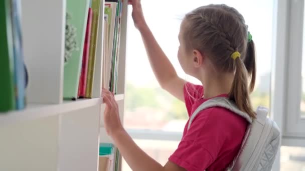 Счастливая школьница ищет книгу в библиотеке — стоковое видео