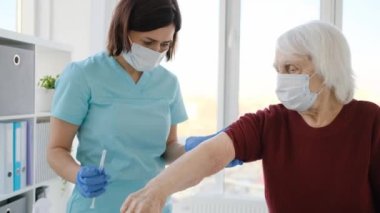 Hemşire yaşlı kadına iğne yapıyor.