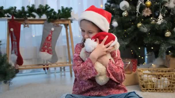 Маленька дівчинка в капелюсі Санта грає з Тедді — стокове відео