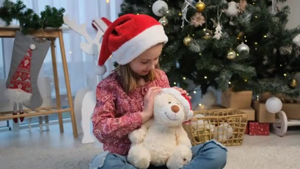 Маленька дівчинка кладе святковий капелюх на іграшку ведмедя — стокове відео