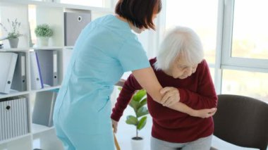 Caregiver supporting old woman to sit on chair