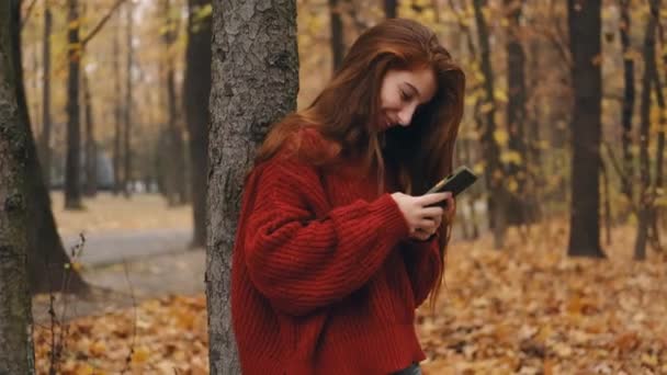 Young girl chatting on smartphone in park — стоковое видео