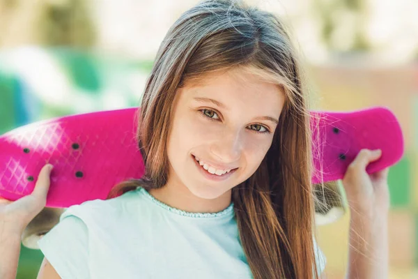 Улыбающаяся девушка держит розовый скейтборд — стоковое фото