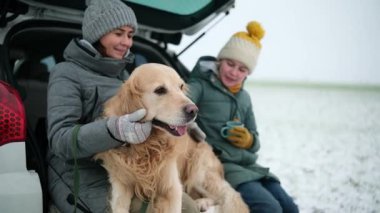 Mutlu bir anne ve kızı, kırsal kesimdeki bir dinlenme tesisinde arabasının bagajında bir köpekle birlikte.