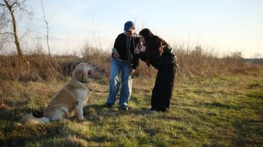 Kızlar dışarıda sevimli Golden Retriever Dog ile oynuyorlar ve fotoğraf çekiyorlar.