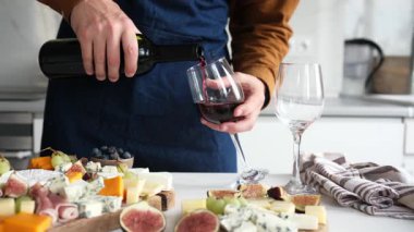 Önlüklü bir adam arkadaşlarıyla bir ev partisi için şarap dolduruyor ve akşam için aperatif olarak peynir tabağı sunuyor.