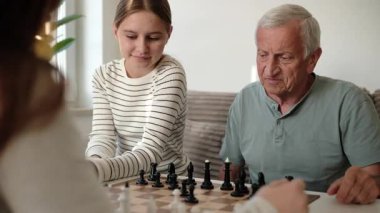 Büyükbabam ve torunlarım satranç oynuyor ve birlikte vakit geçiriyorlar.