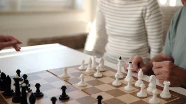 Büyükbabam torunlarıyla satranç oynuyor ve kızlara kuralları öğretiyor.