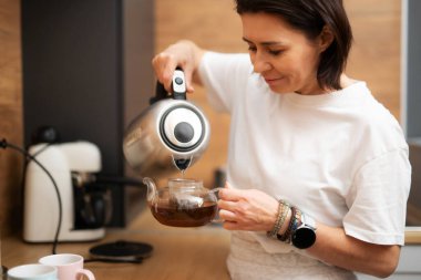 Girl Pouring Boiling Water Into Teapot With Black Tea In The Kitchen For Breakfast