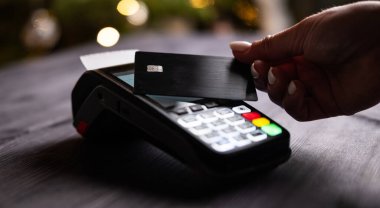 Kablosuz Pos terminali ile kredi kartıyla ödeme yapan kız, bulanık bir Noel arkaplanına karşı