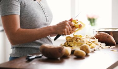 Mutfakta çiğ patates soyan ve diğer sebzeleri bıçaklayan bir kız.
