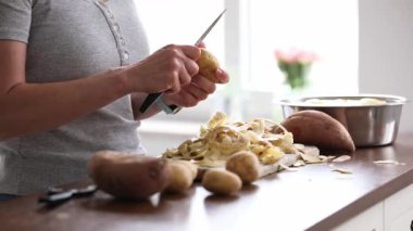 Woman Peeling Raw Potatoes And Vegetables With A Knife In The Kitchen