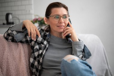 Evdeki koltukta oturan bir kadın telefonda konuşuyor.