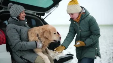 Mutlu anne ve kız, bir kış durağında bagajda altın av köpeğiyle oynuyorlar.