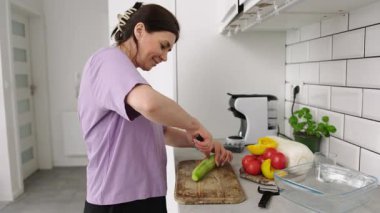 Mutfaktaki kız sebze salatası için salatalık kesiyor.