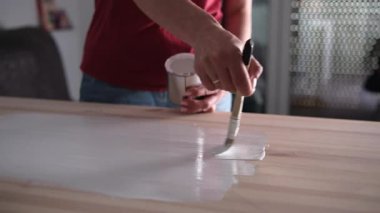 Bir kadın, tahta bir masa yüzeyini fırçayla boyuyor.