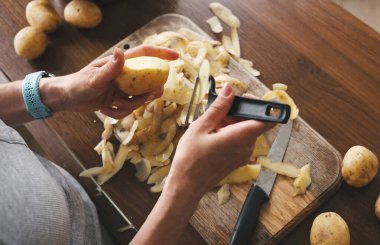 Patates soyacağı ve diğer çiğ sebzelerle çiğ patates soyan bir kadın.