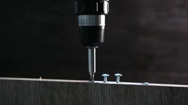 Matkap, çalışma alanındaki tahta bir tahtaya vida takıyor.