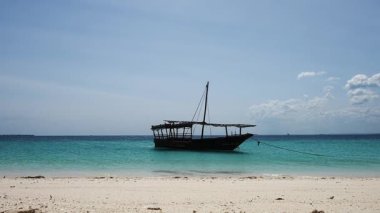 Geleneksel ahşap balıkçı teknesi güneşli bir günde kumsalda dinleniyor.