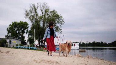 Kız, kumsalda sevimli, altın bir köpekle yürüyor.