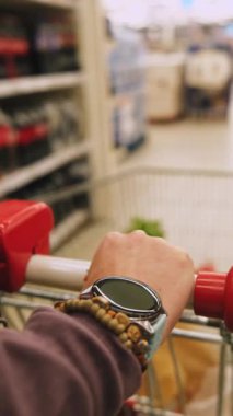 Marketteki içki reyonunda, markette alışveriş arabasıyla market alışverişi yapan bir kadın.