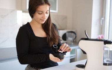 Genç kız sabah vakti mutfakta kahve kapsülleriyle kahve yapmaya hazırlanıyor..