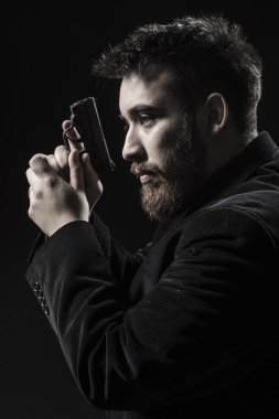 Top sakallı genç adam silahla sola bakacak şekilde