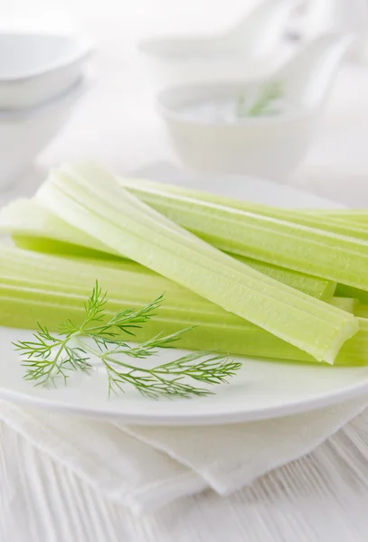 Fresh celery sticks with yogurt dip on white wooden background