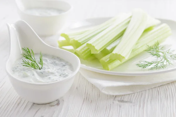 Fresh celery sticks with yogurt dip on white wooden background