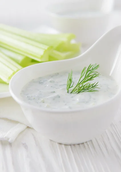 Fresh celery sticks with yogurt dip on white wooden background