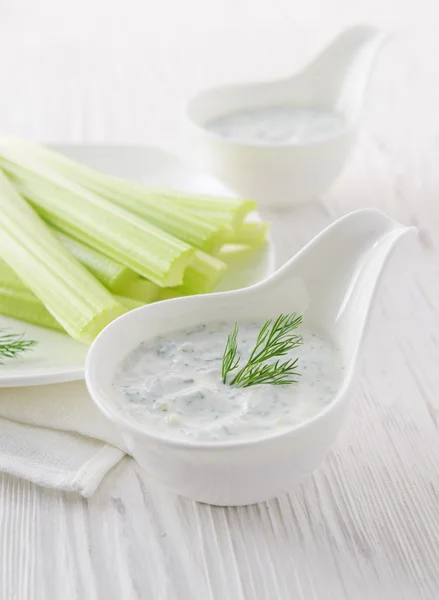 Fresh celery sticks with yogurt dip on white wooden background