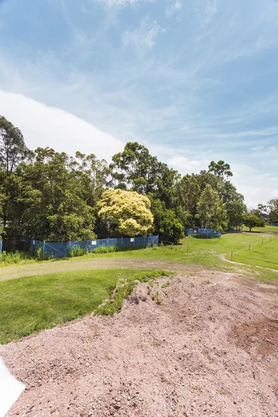 A field with a forest in far rounded by a blue fence — Stock Photo, Image