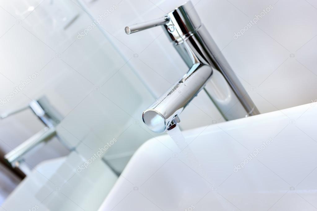 Running water of a modern faucet in the washroom with washstand 