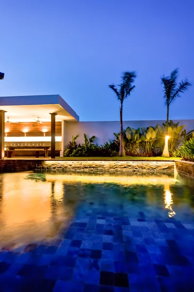 Piscina de agua de lujo y jardín con zona de comedor por la noche — Foto de Stock